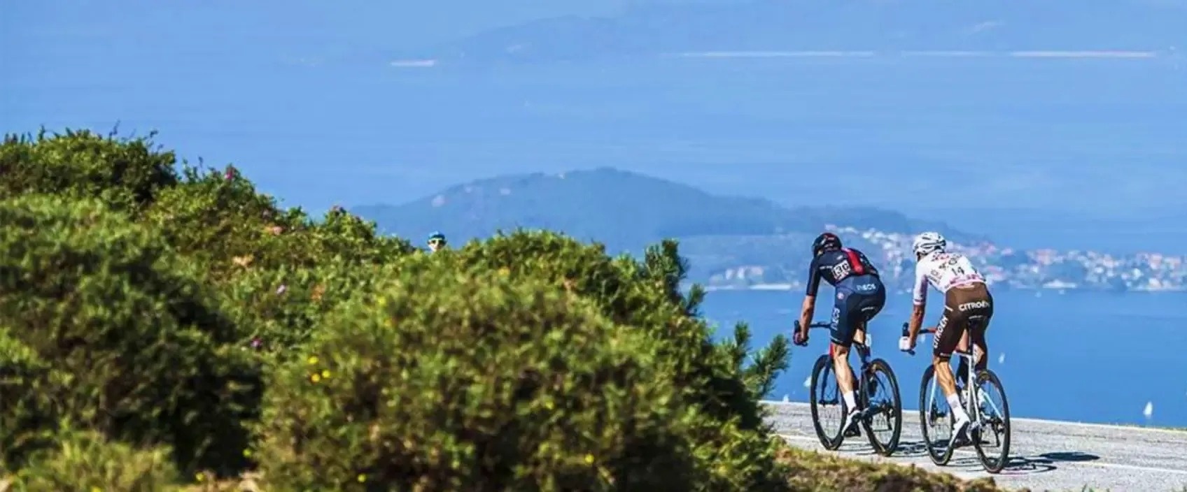 two people are riding bicycles down a hill near the ocean .