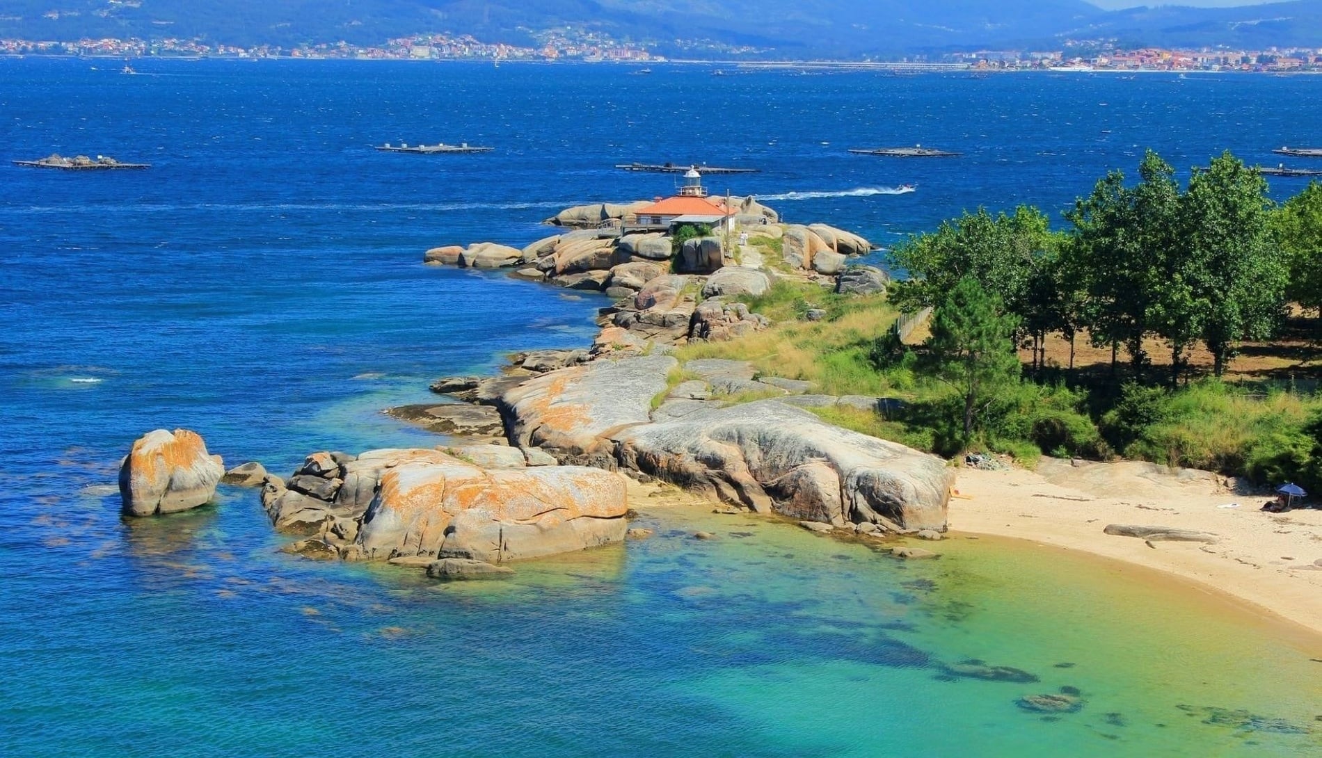 a rocky shoreline with boats in the water and mountains in the background
