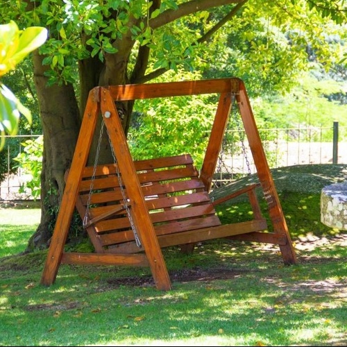 a wooden swing sits under a tree in a park