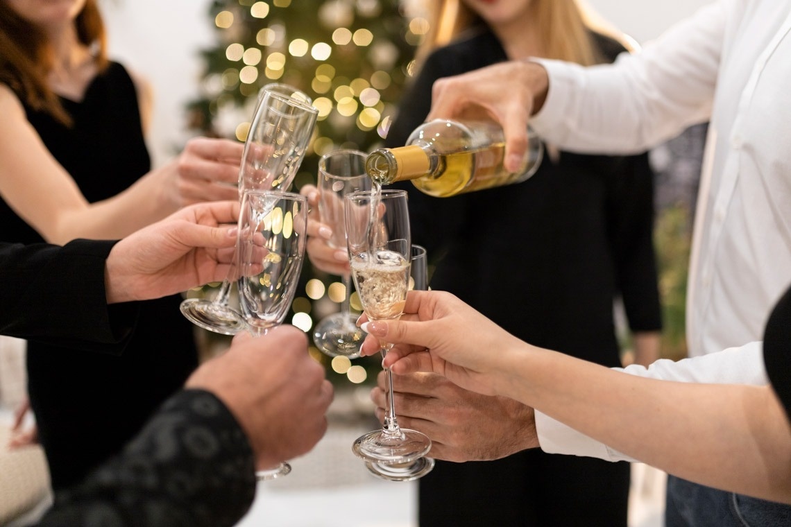 a group of people toasting with champagne in front of a christmas tree