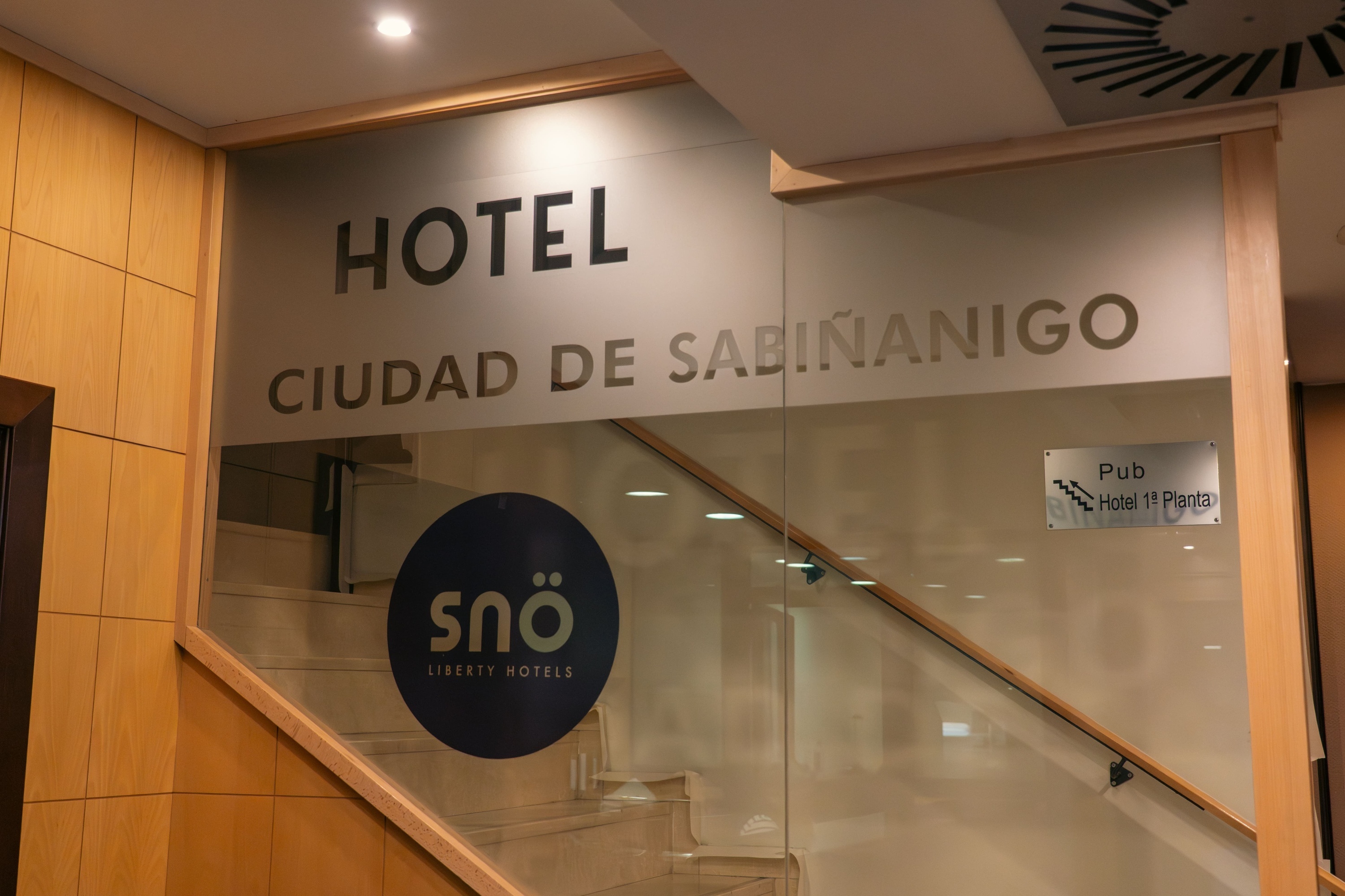 Entrada al Hotel Ciudad de Sabiñánigo, con logo Snö, escalera y señalización a pub y habitaciones.