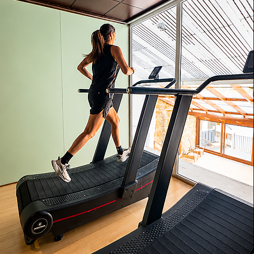 Woman running on a SNO: Villa de Sallent 4* treadmill in a modern gym with large windows.