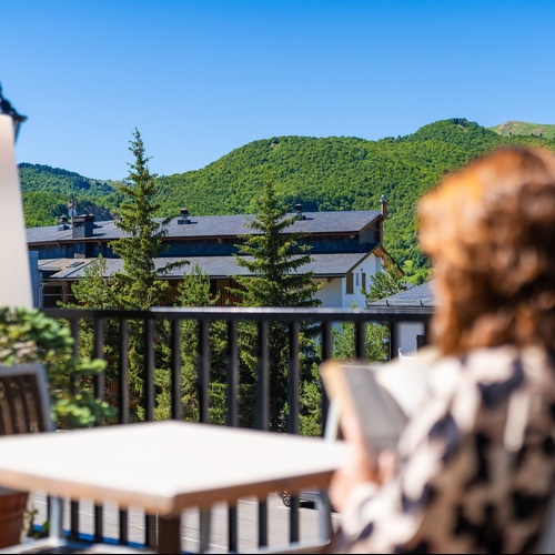 una mujer lee un libro en un balcón con vistas a las montañas