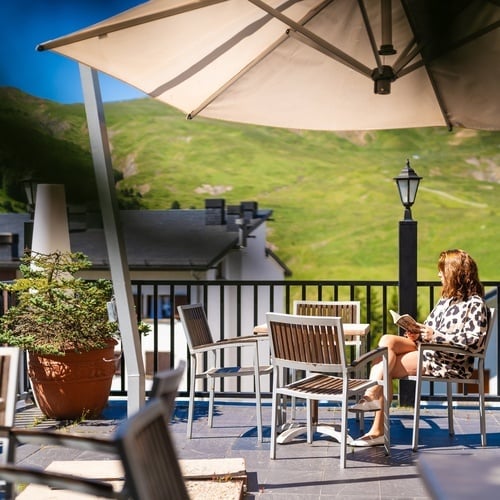 a woman sits on a balcony under an umbrella reading a book