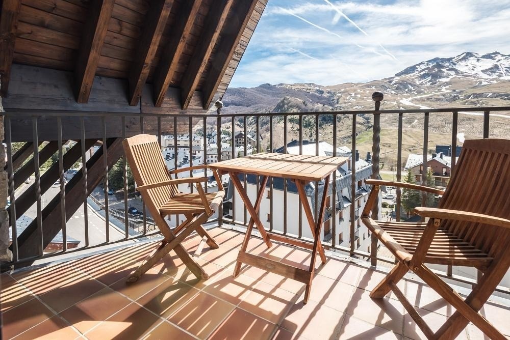 una mesa de madera y dos sillas en un balcón con vistas a las montañas