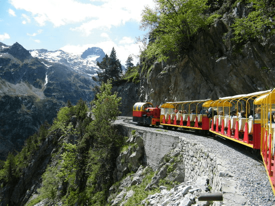 un train rouge et jaune traverse une vallée avec des montagnes en arrière-plan