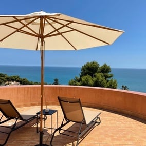 Liegestühle und ein Sonnenschirm auf einem Balkon mit Blick auf das Meer