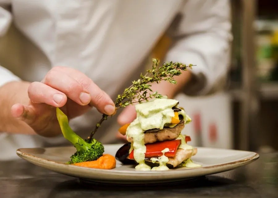 a chef is adding broccoli to a plate of food