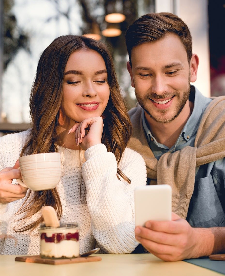 a man and woman sit at a table looking at a cell phone