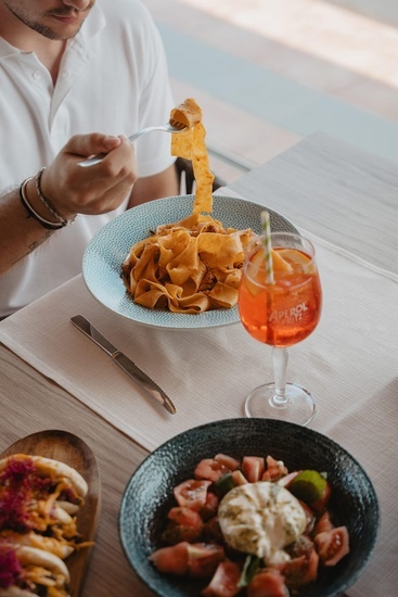 ein Mann isst Nudeln neben einem Glas aperol spritz