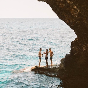 tres hombres de pie en una roca en el océano