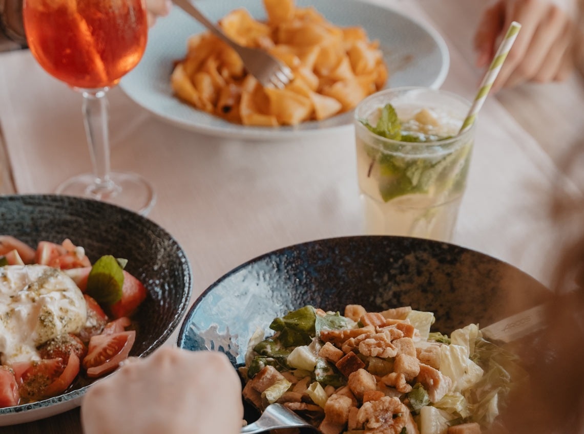 una persona está sentada en una mesa con platos de comida y bebidas .