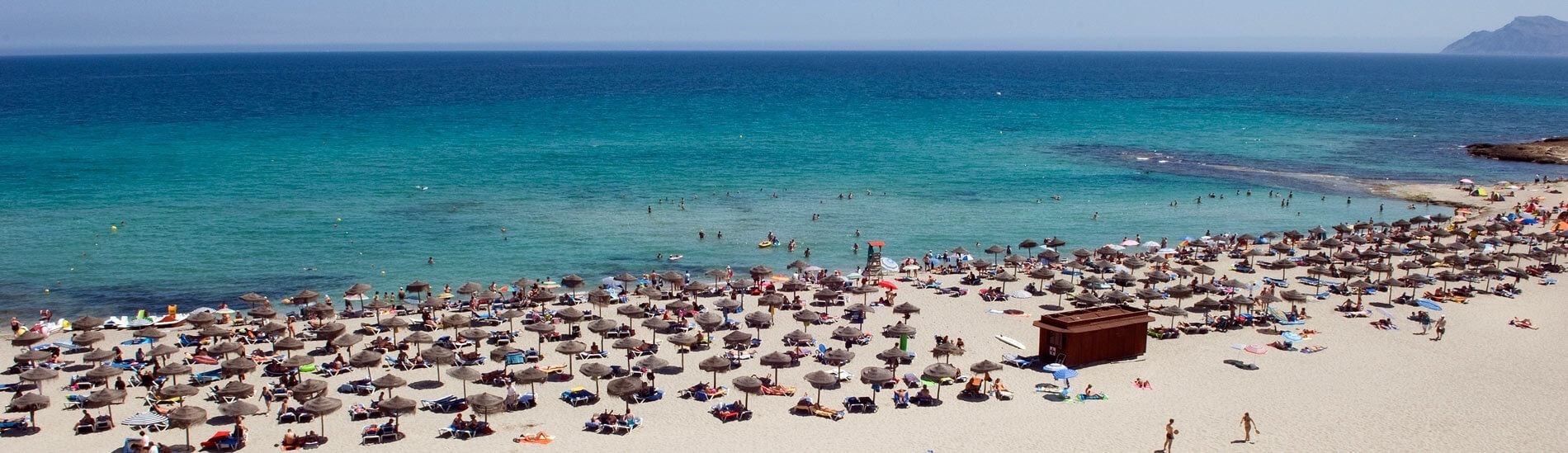una playa llena de gente y sombrillas con una red de voleibol en la arena