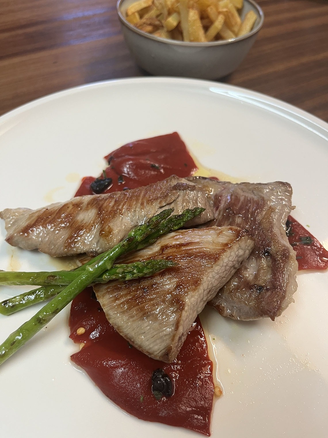 een bord vlees en groenten met een kom frietjes op de achtergrond