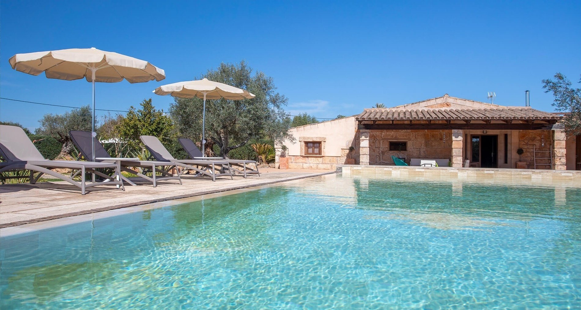 a swimming pool with chairs and umbrellas in front of a house