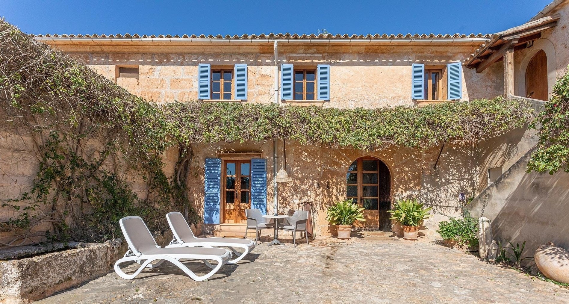 two lounge chairs sit in front of a building with blue shutters