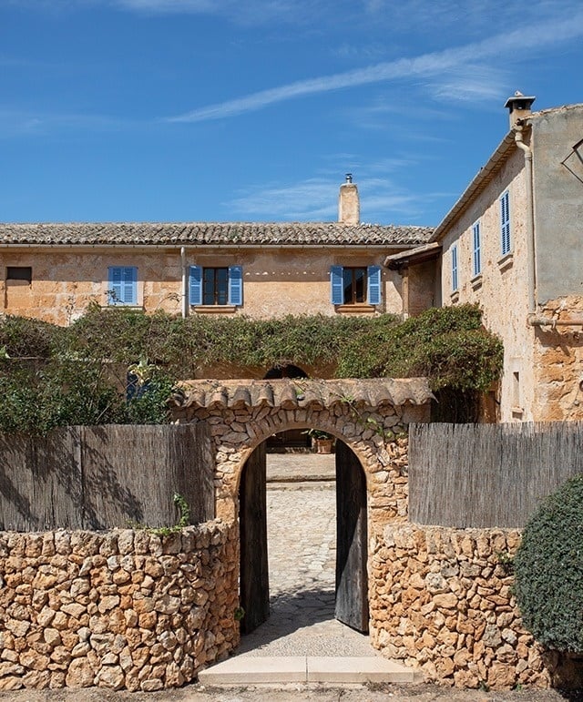 a stone archway leads to a house with blue shutters