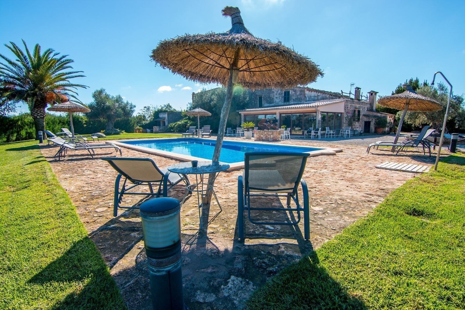 una piscina rodeada de sillas y sombrillas con una casa en el fondo