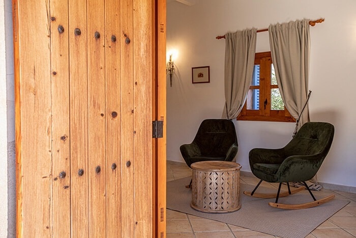 een houten deur opent naar een kamer met twee schommelstoelen en een tafel