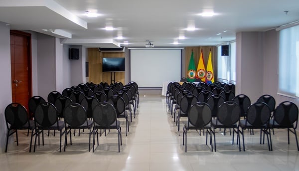 una sala de conferencias llena de sillas negras y una pantalla