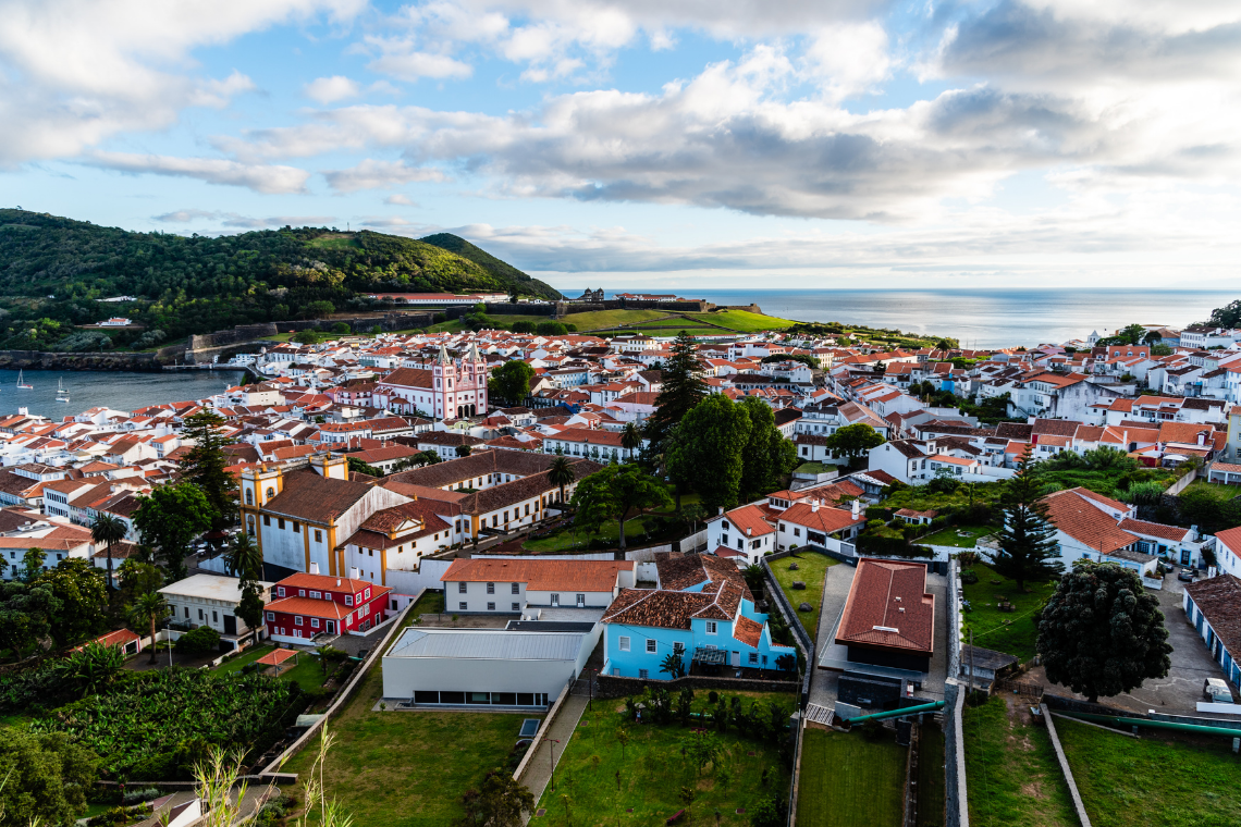 Vista panorâmica da cidade com casas brancas e telhados vermelhos, mar azul e colina verde. Sul Villas & Spa