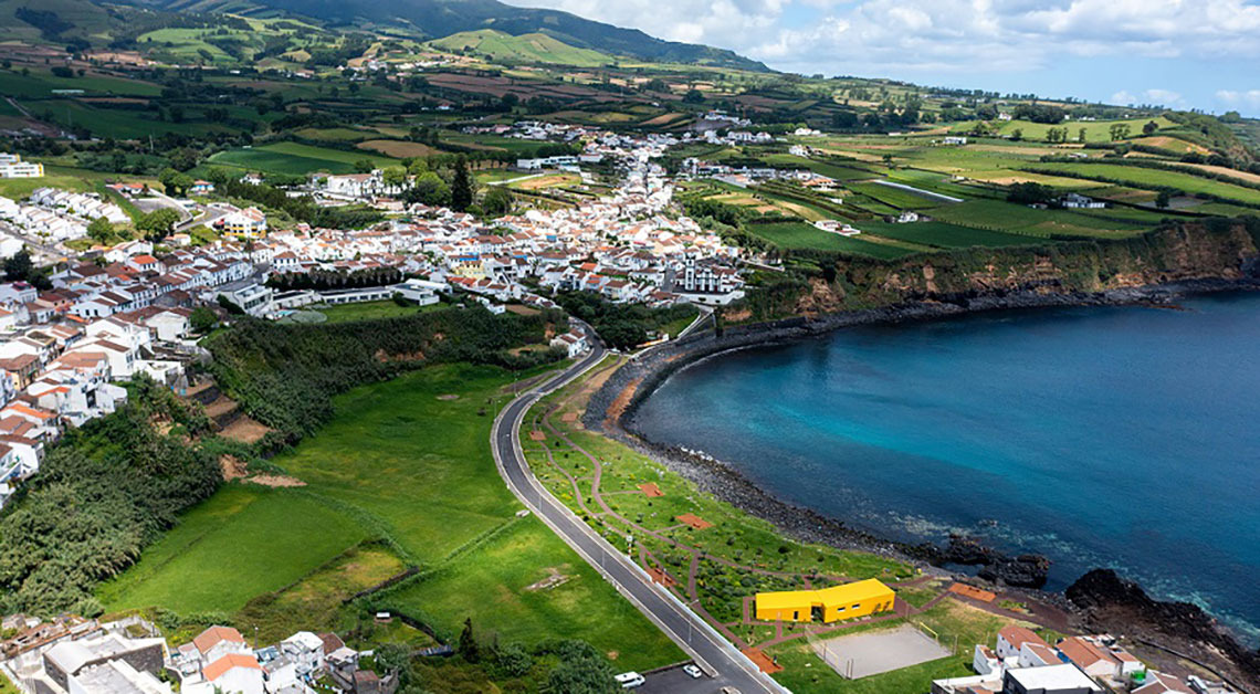 Aerial view of a coastal village and hotel Sul Villas & Spa with turquoise waters and lush green hills.