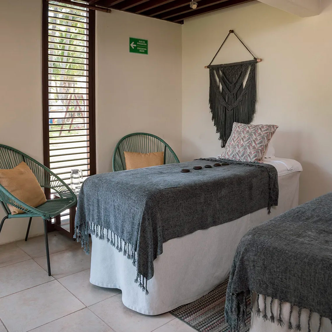 Camillas de masaje en Laguna Suites con manta gris, cojín decorativo y arte macramé.