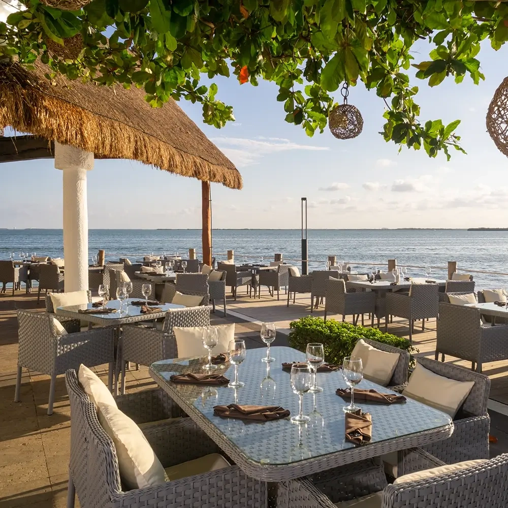 Restaurante frente al mar en Sunset World Resorts: Corporativa. Mesas, sillas y vista al océano.