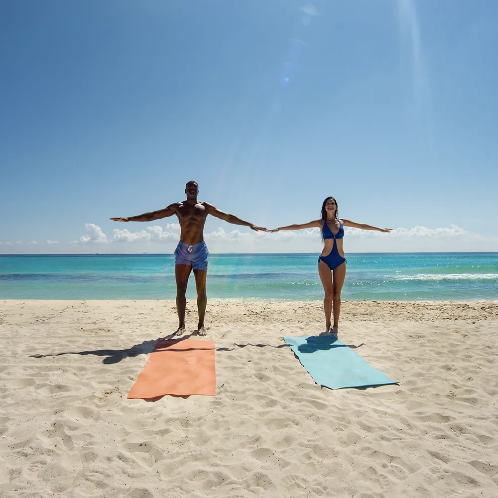 Pareja en yoga playero con el mar turquesa, ideal para eventos corporativos de Sunset World Resorts: Corporativa.