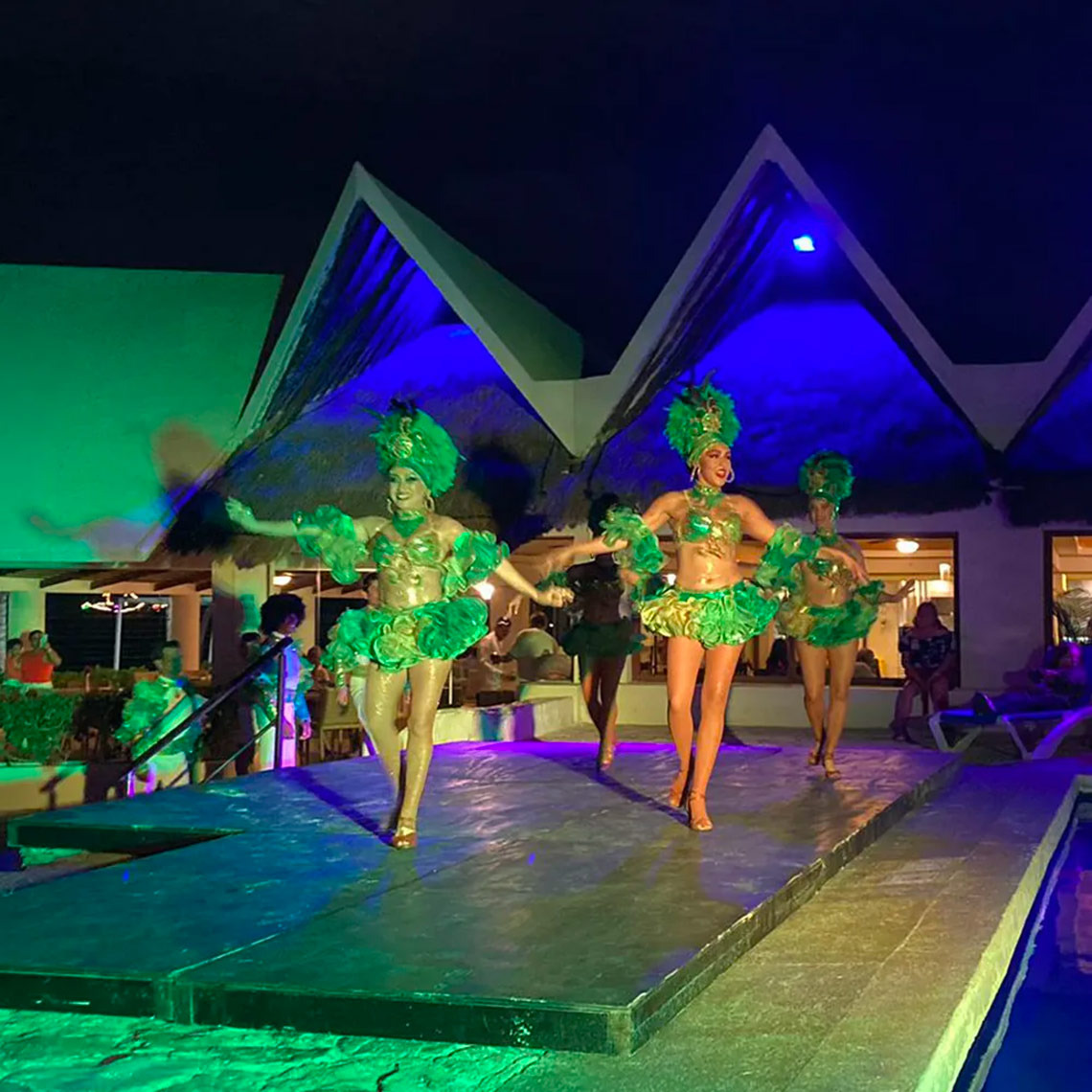 Laguna Suites | Página Oficial: Espectáculo de bailarinas con trajes brillantes en una tarima nocturna.