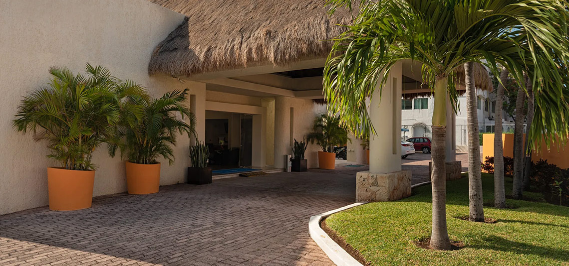Entrada tropical de Laguna Suites | Página Oficial con palmeras y techo de paja.