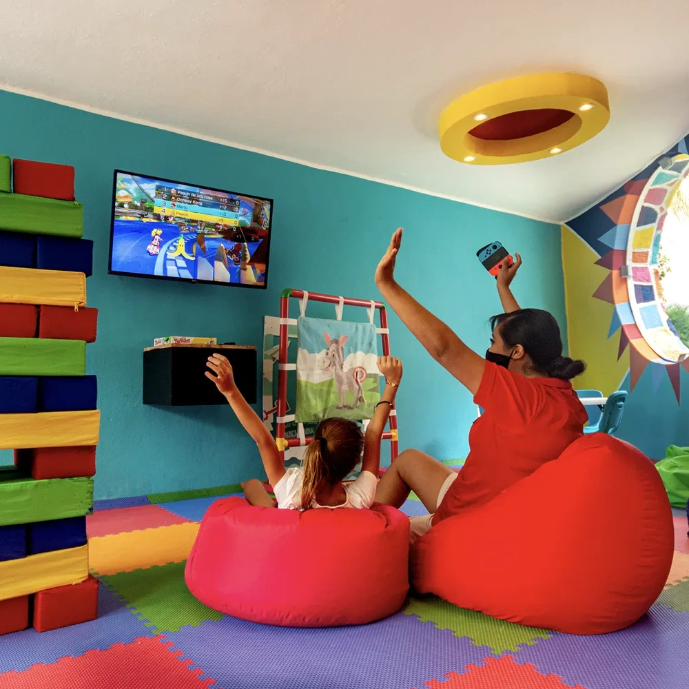 Sunset World Resorts: Corporativa - Kids play video games on beanbags, enjoying a colorful resort room.
