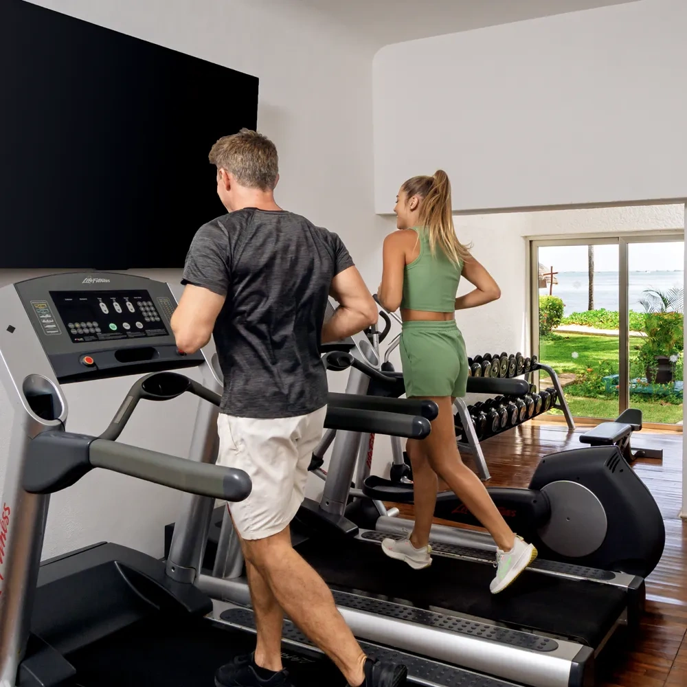 Pareja ejercitándose en gimnasio con vista al mar en Sunset World Resorts