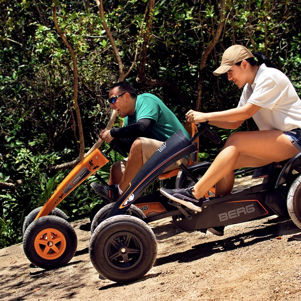 Two people enjoy a Sunset Hotels Collection: Corporativa adventure on go-karts through a wooded trail.