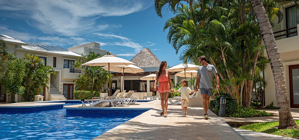 Familia pasea por Laguna Suites, con piscina y palmeras.