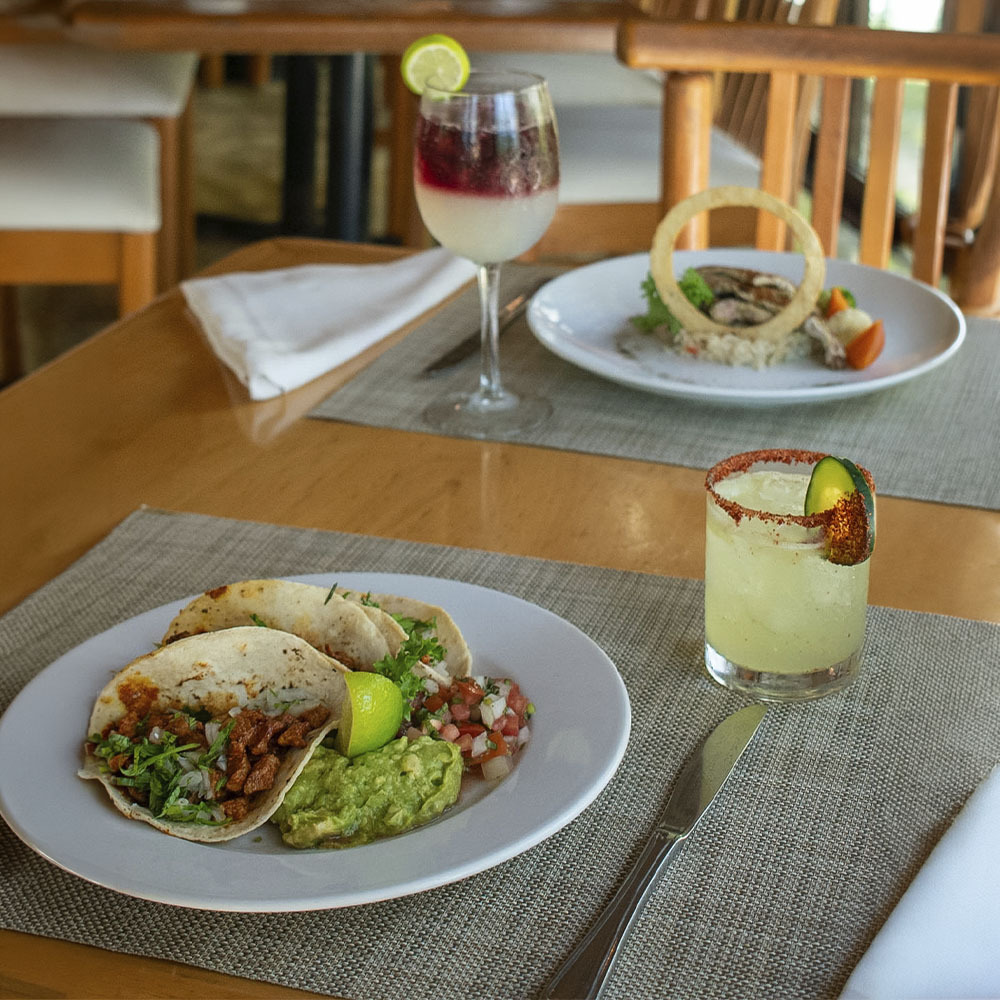 Sunset World Resorts: Corporativa - Tropical restaurant with thatched roof, wooden tables, and chairs.