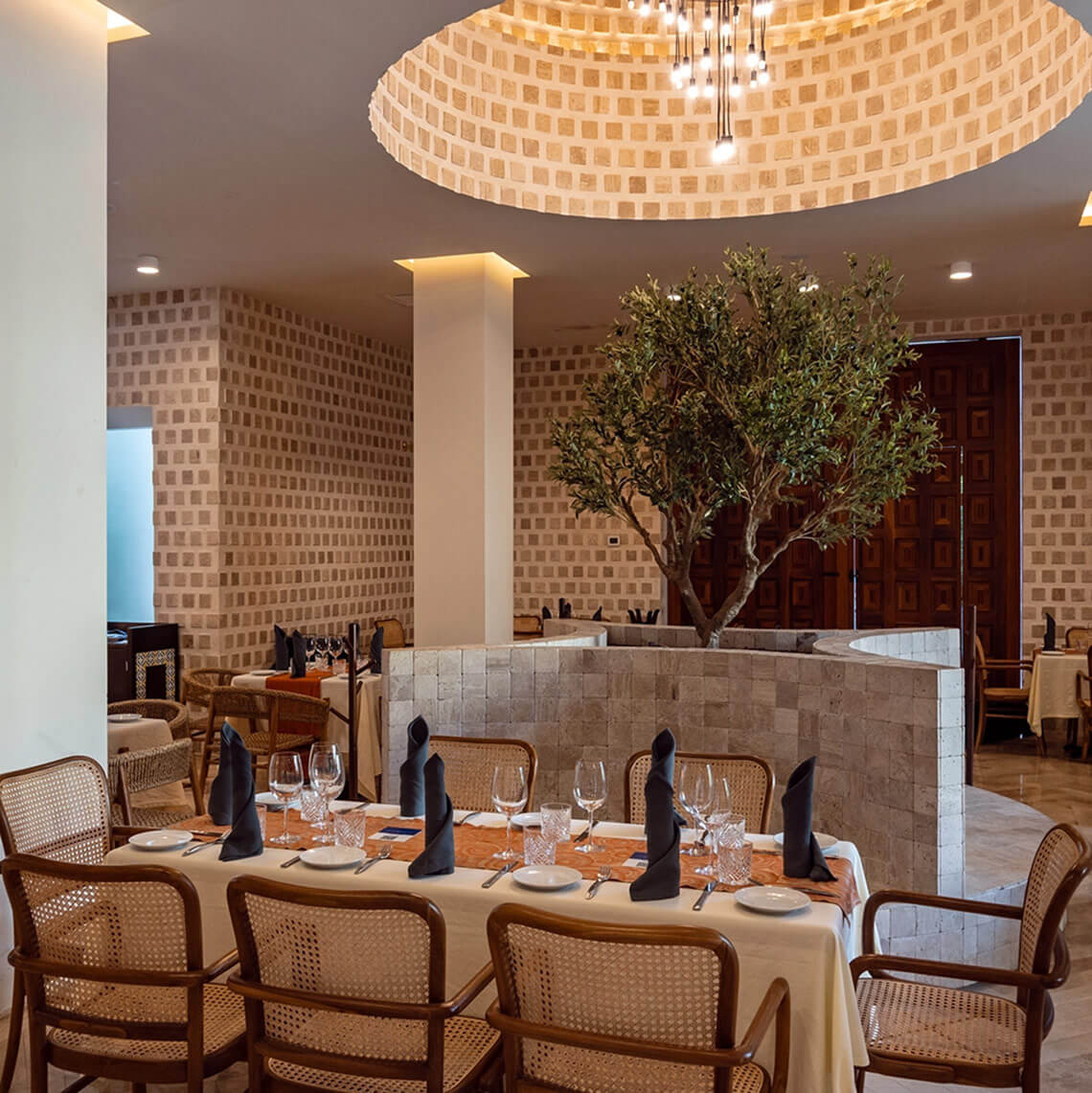 Elegant dining room at Hacienda Tres Rios with set tables and a central olive tree.