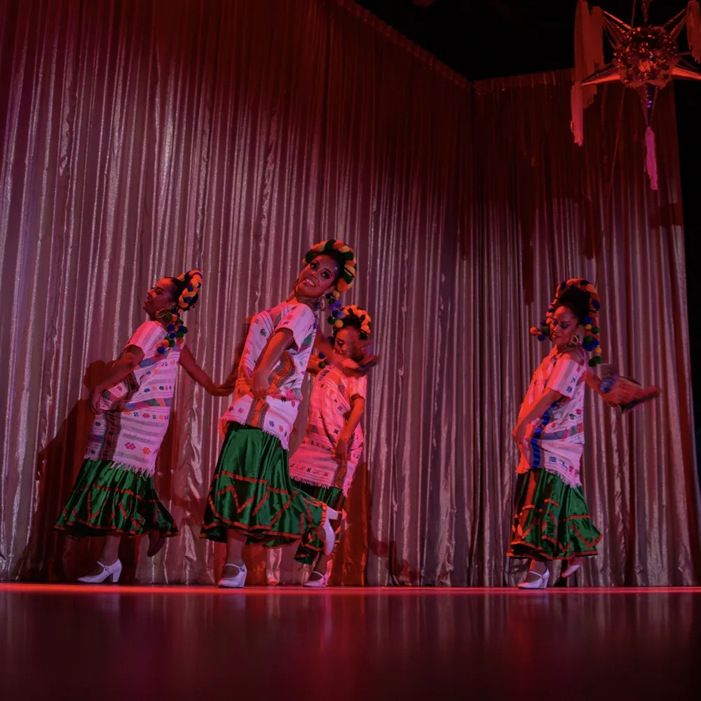 Dancers in traditional clothing perform on stage, with a festive piñata overhead. This is a great entertainment option at our Sunset Hotels Collection: Corporativa.