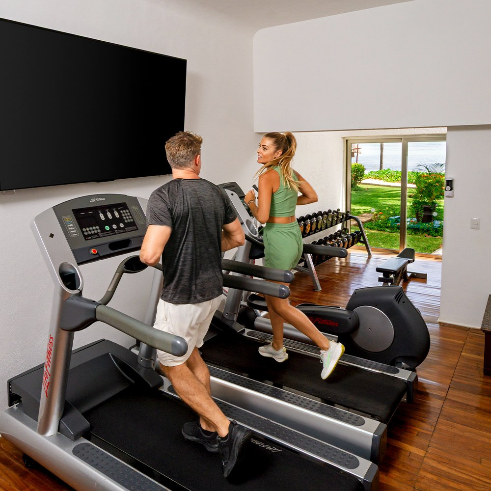 Pareja ejercitándose en gimnasio con vista al mar en Sunset World Resorts