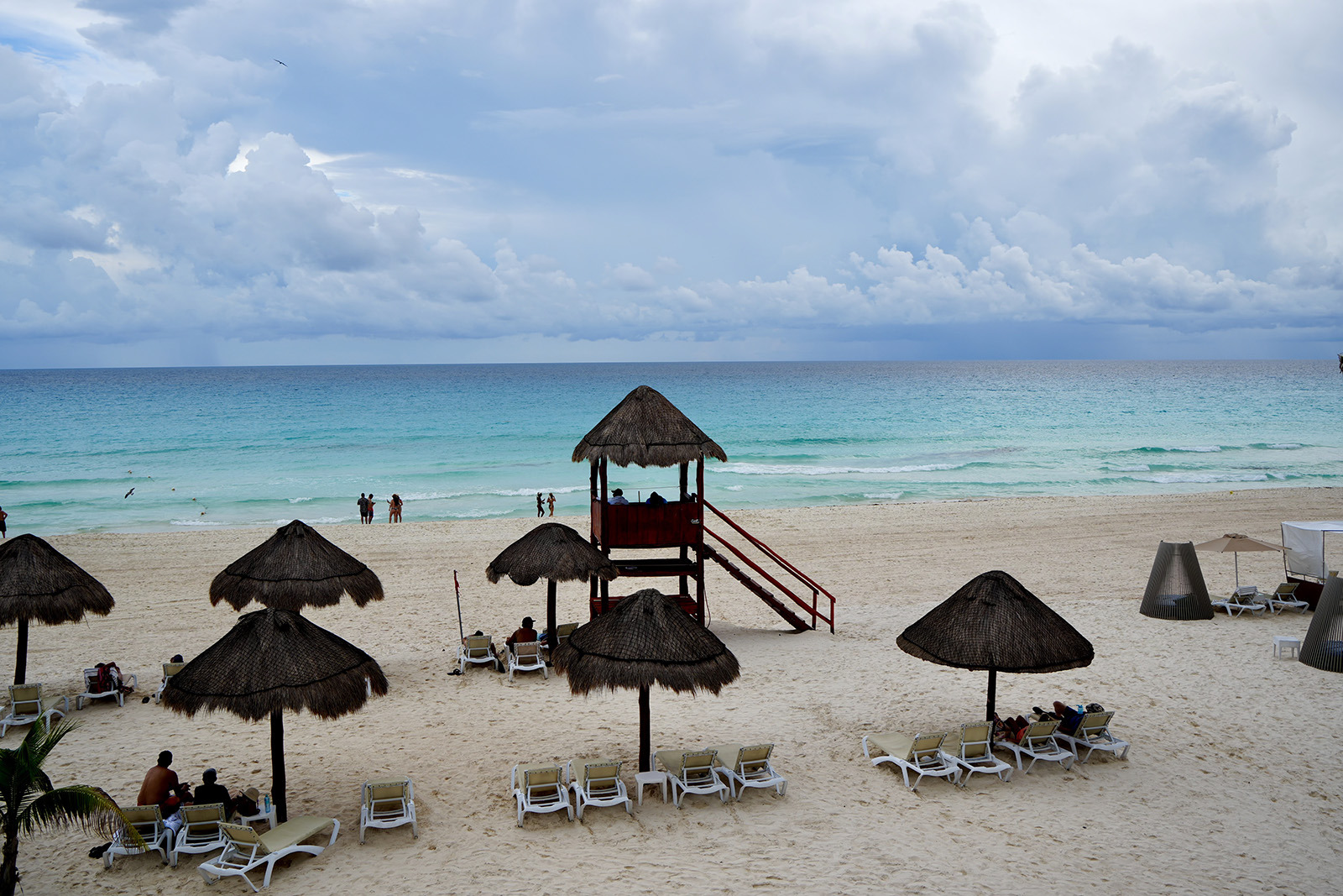 Sunset Hotels Collection: Corporativa: Palapa y reposeras en playa turquesa con sombrillas de paja y puesto de socorrista