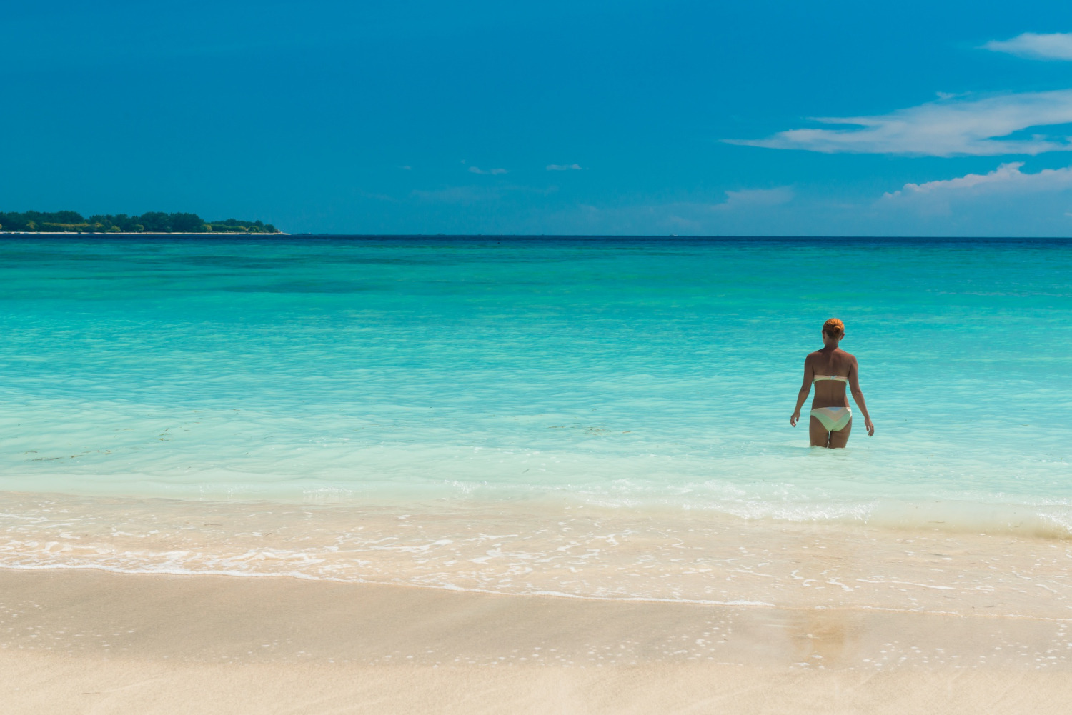 Woman in bikini entering turquoise ocean from sandy beach, Sunset Hotels Collection: Corporativa.