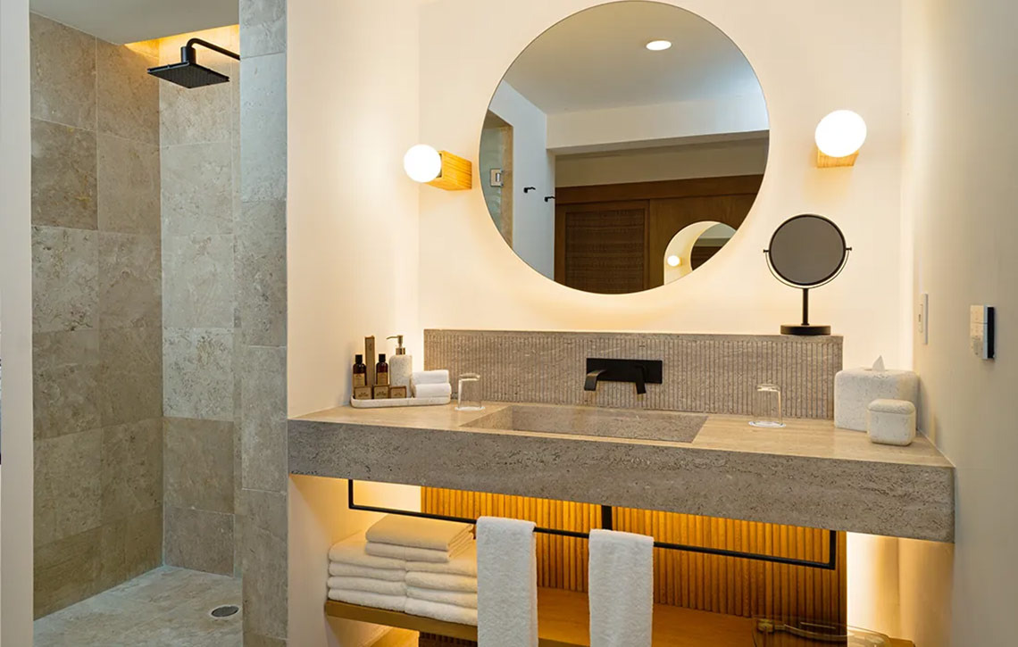 Modern hotel bathroom with stone vanity, large mirror, and shower at Hacienda Tres Rios.