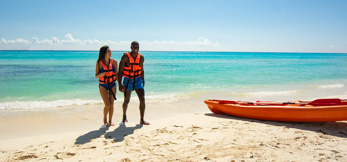 Pareja con chalecos salvavidas en la playa, junto a un kayak en Sunset Fishermen Beach Resort.