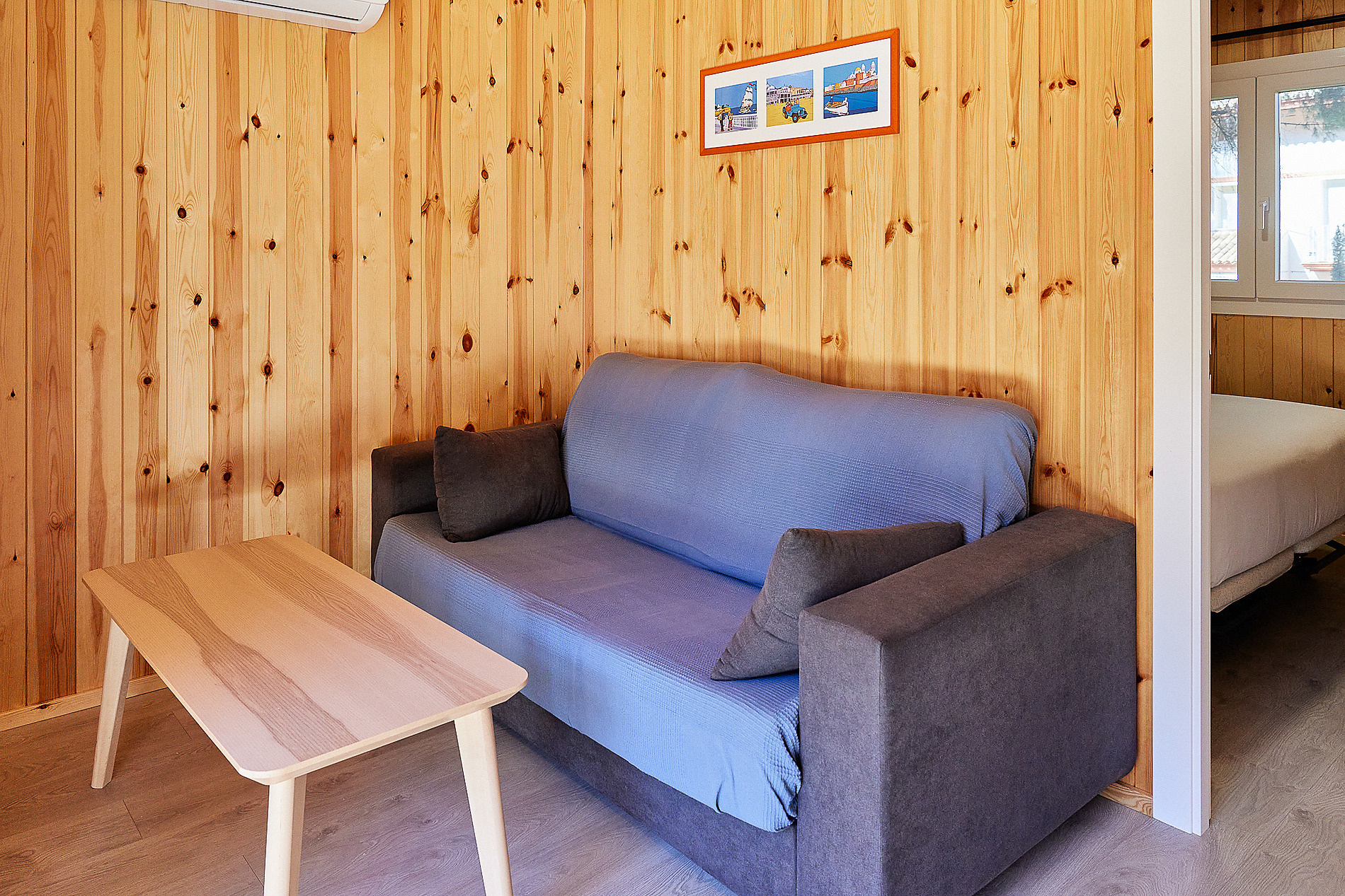 Sofá azul y mesa de madera en sala de estar de Taiga: Puerto Santa Maria, con cama visible al fondo.