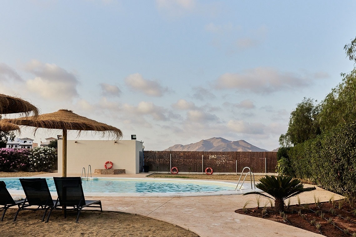 a swimming pool surrounded by chairs and umbrellas with mountains in the background