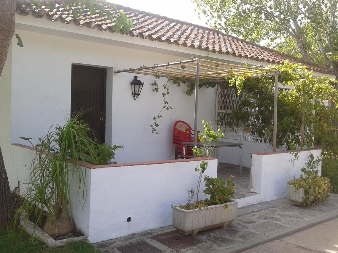 una pequeña casa blanca con una mesa y sillas rojas en el porche