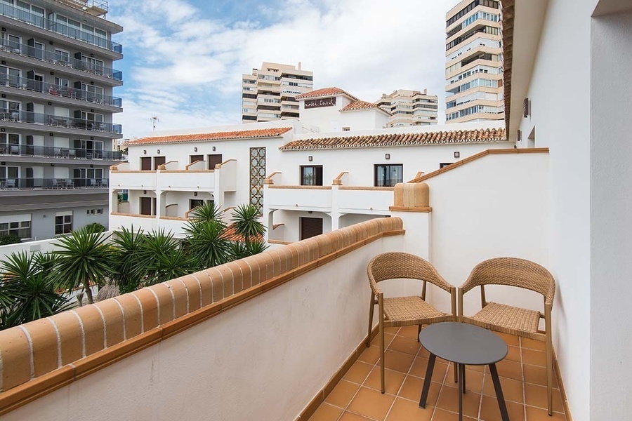 un balcón con dos sillas y una mesa frente a un hotel