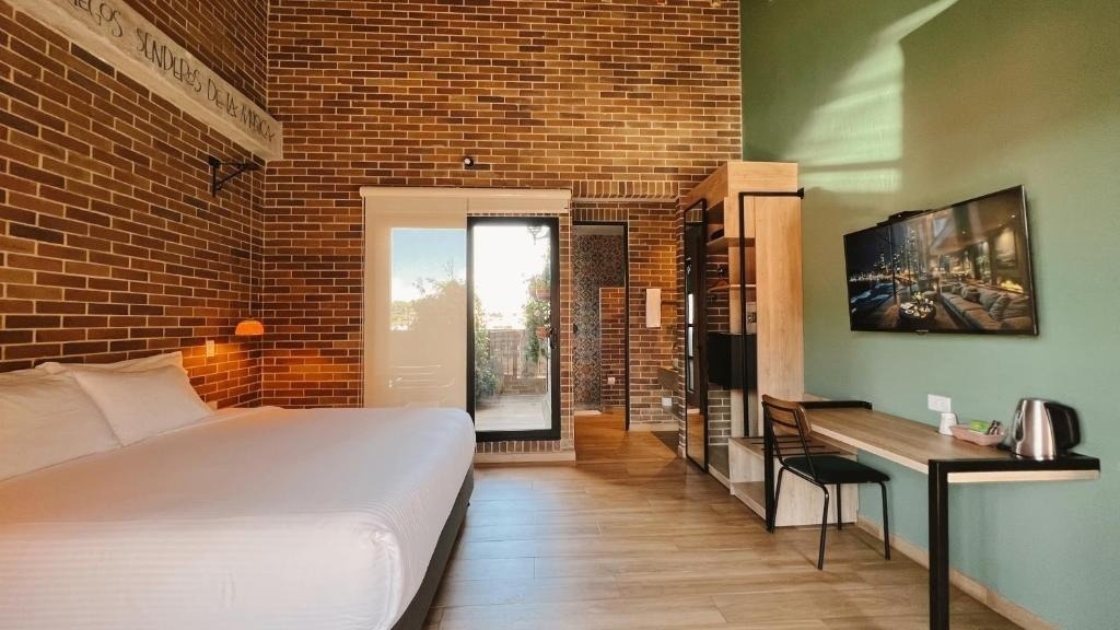 Modern hotel room with brick walls, king bed, and TV at Casa Rosé Hotel.