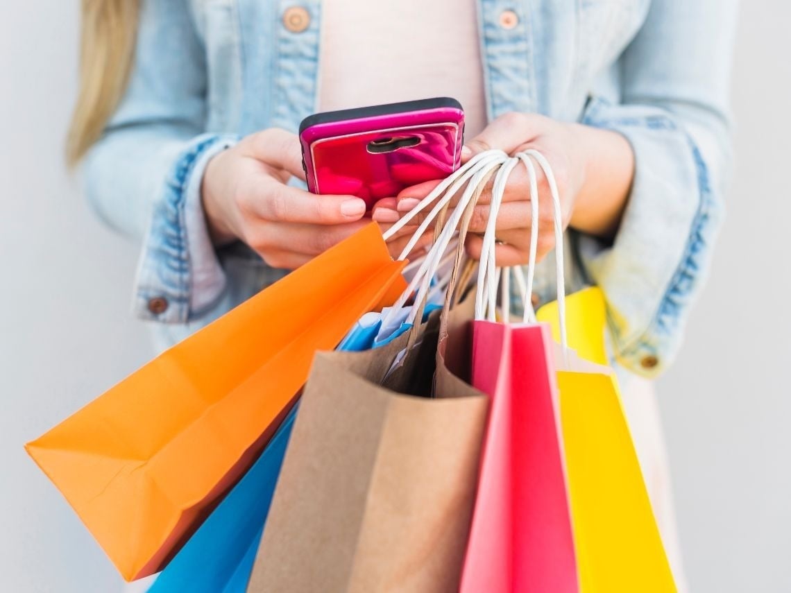 Mujer revisa su móvil rodeada de bolsas de compras, Tequendama Corporativa