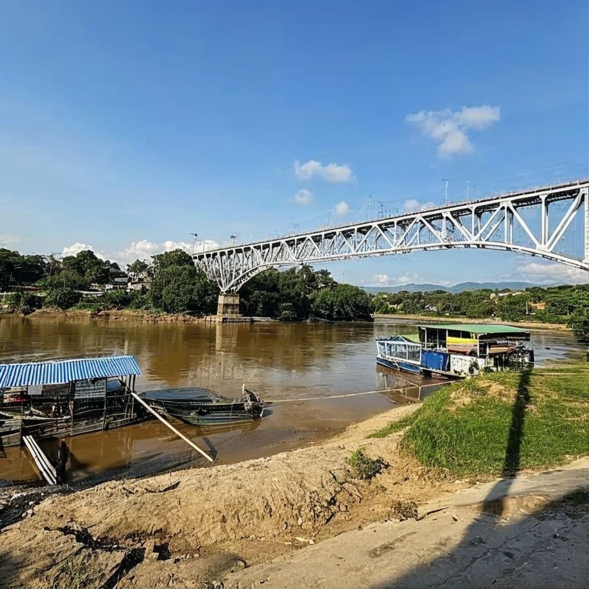 Puente metálico sobre río marrón con barcos, vistas a Tequendama: Corporativa.